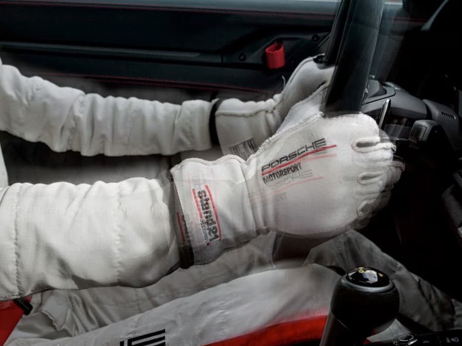 View into the cockpit of a Porsche 911 GT3 RS. A person wearing a racing suit and gloves is holding the steering wheel.